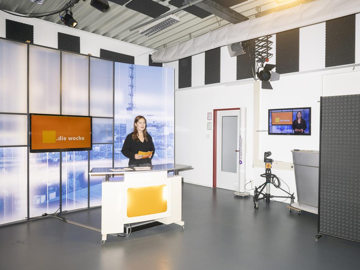 Eine Frau steht vor einem Fernsehbildschirm.