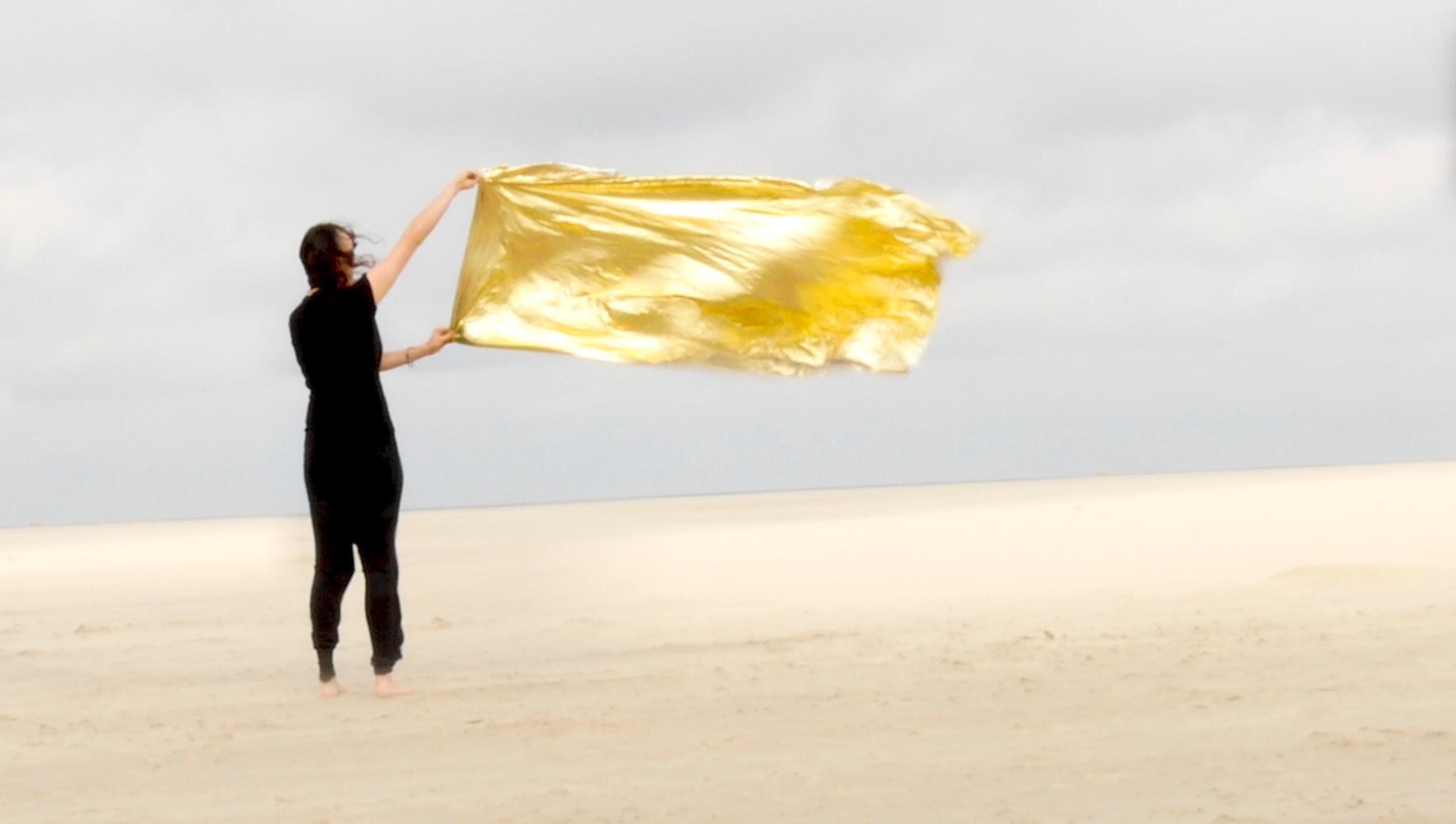 Eine schwarz gekleidete Frau mit einer gelben Flake auf Strand